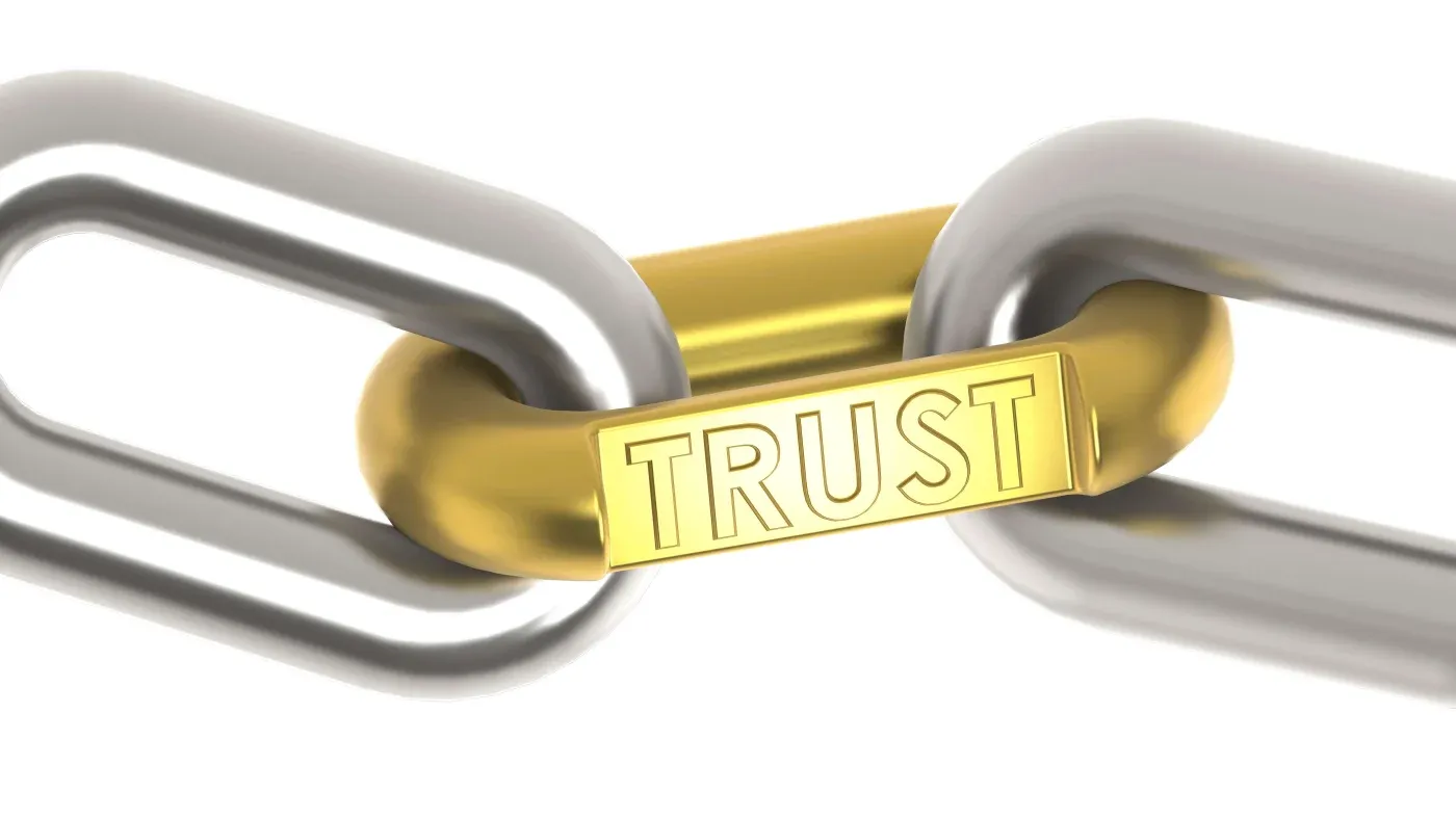 A metallic chain with a central gold link engraved with "TRUST," symbolizing strength and connection. The tone is secure and reliable.