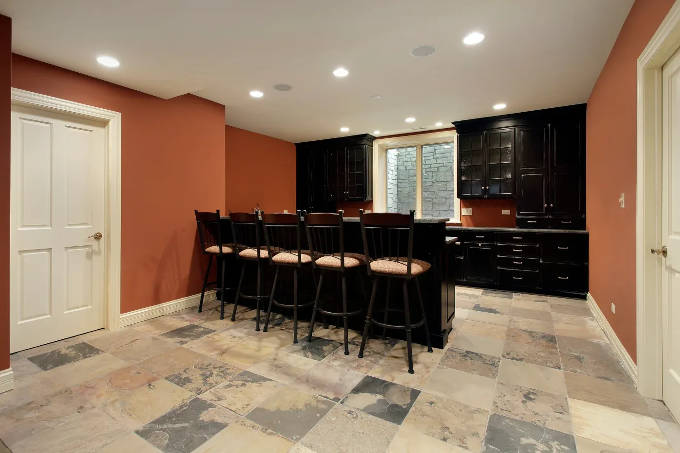 A cozy kitchen with warm terracotta walls, dark wood cabinets, and a central island with high chairs. Rustic tile flooring adds a touch of elegance.