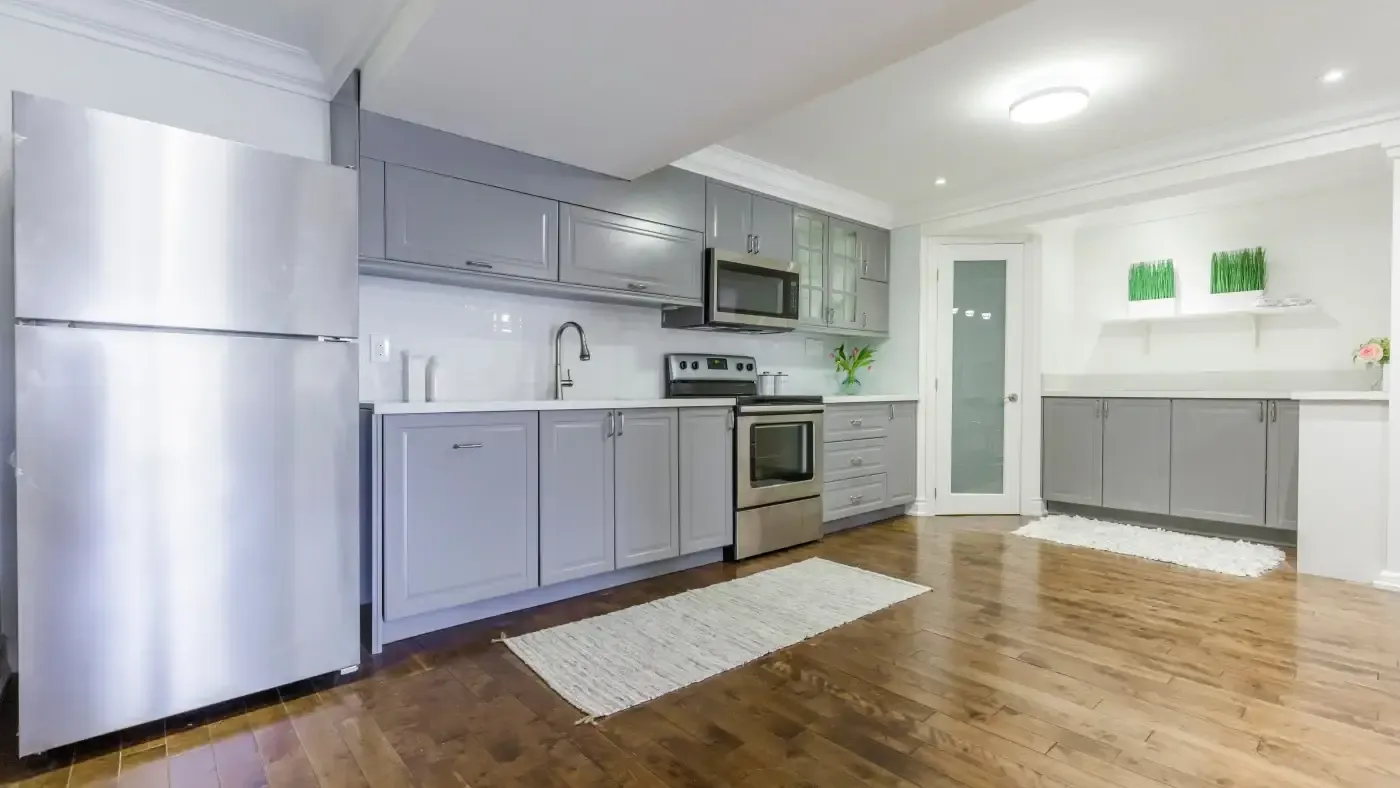 Modern kitchen with gray cabinets and stainless steel appliances, including a fridge and oven. Hardwood floors and soft lighting create a warm, inviting atmosphere.