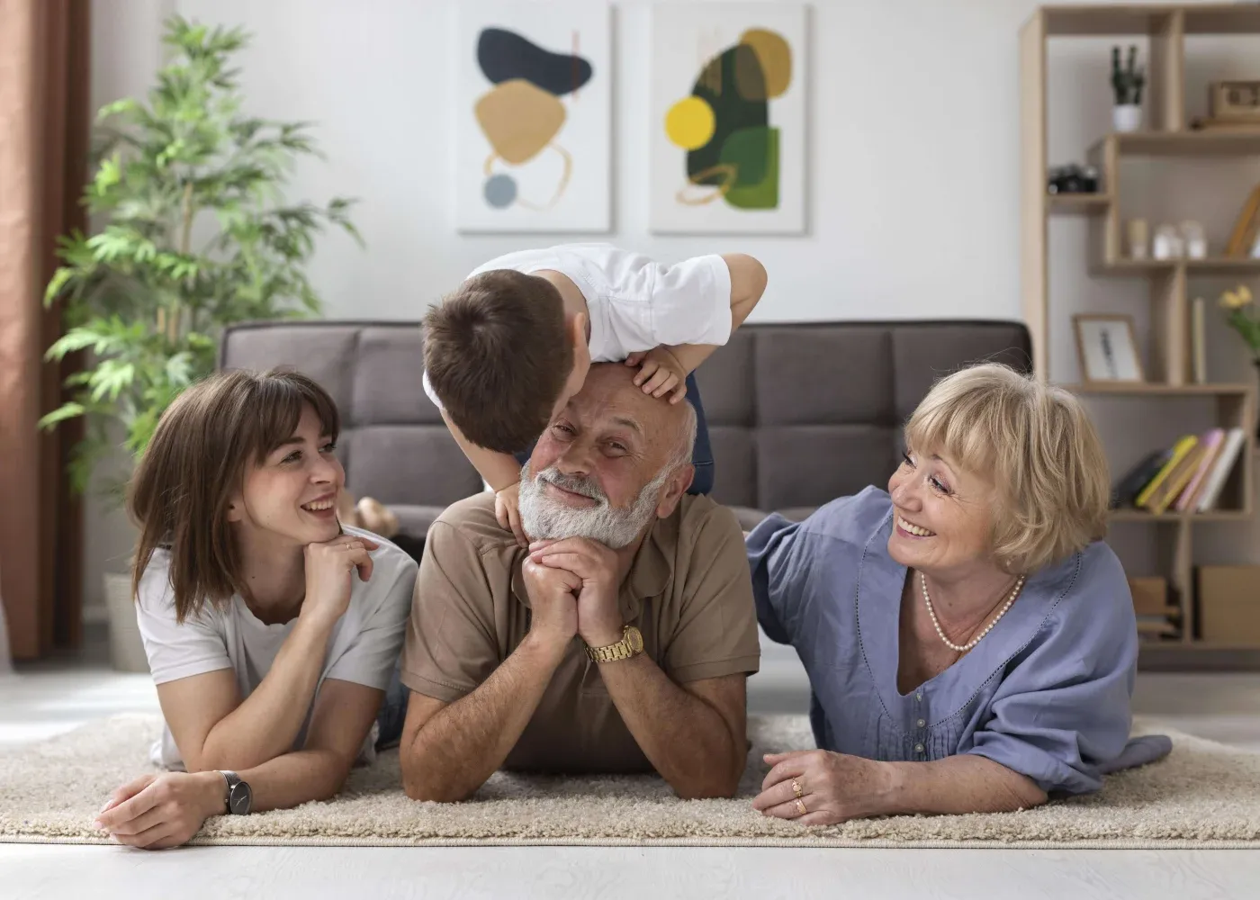 A joyful family scene with three adults and a child on a living room floor. The child playfully kisses the bearded man's cheek, creating a warm atmosphere.