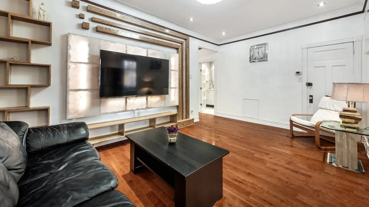 Stylish living room with hardwood floor, black leather sofa, TV on backlit wall panel, modern shelving, a dark coffee table, and a cozy armchair.