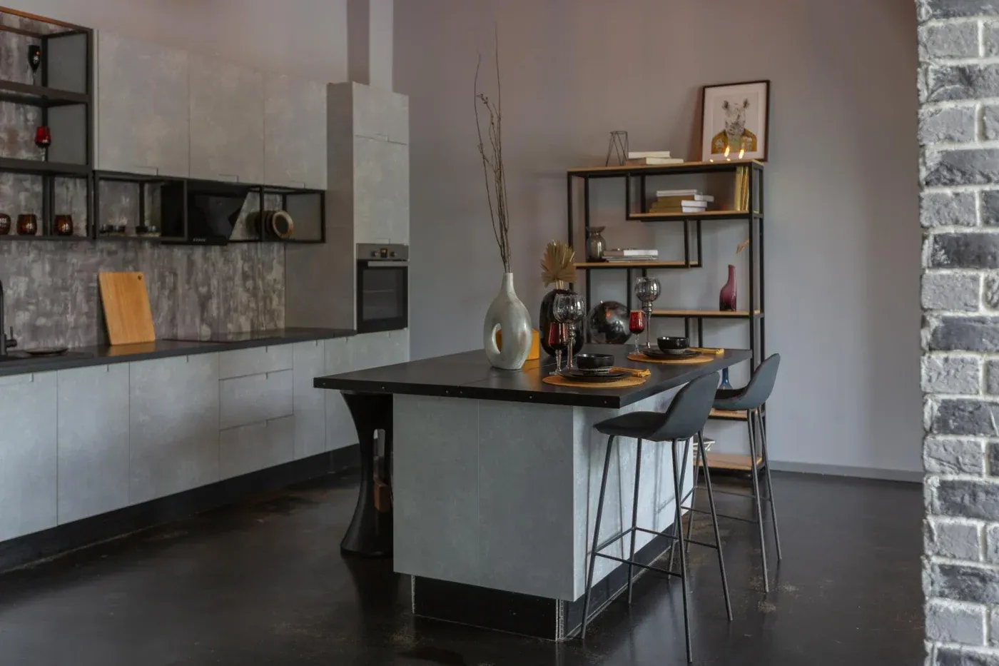 Modern kitchen with gray cabinets, black countertops, and a matching island. Open shelving holds decor items. Two stools at the island. Minimalist and sleek design.