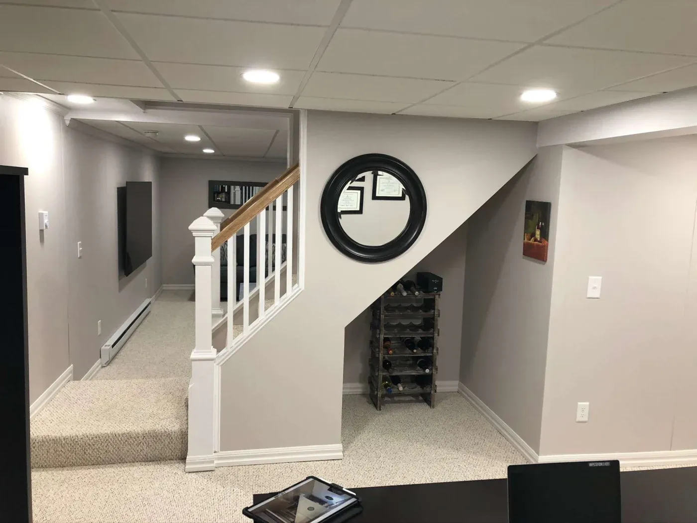 Basement room with a staircase, round mirror on the wall, and a wine rack underneath. Soft lighting and neutral tones create a cozy atmosphere.