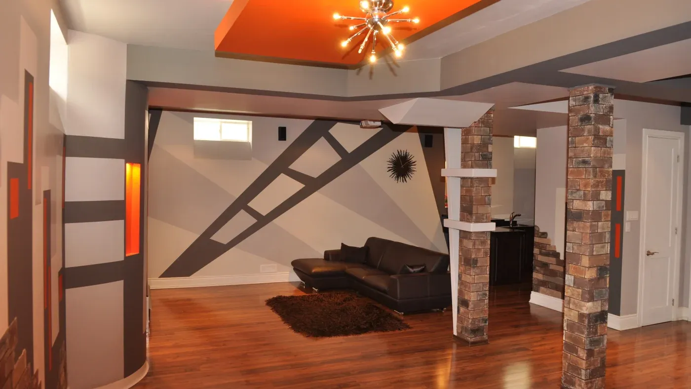 Modern room with geometric wall patterns, gray and orange colors, brick columns, hardwood floors, and a starburst ceiling light. Cozy yet stylish ambiance.