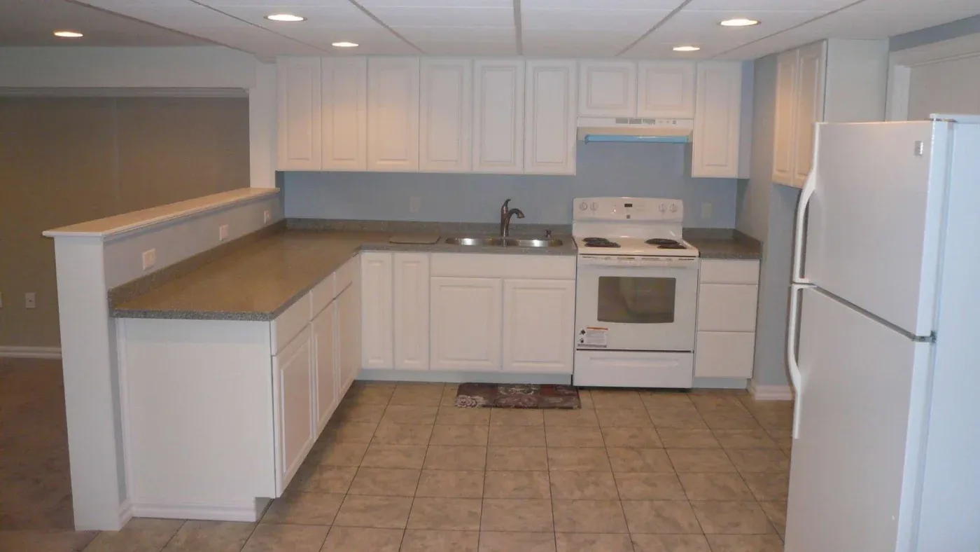 A spacious kitchen with white cabinets and appliances, gray countertops, and tiled floors. The room has a modern and clean ambiance with ample lighting.