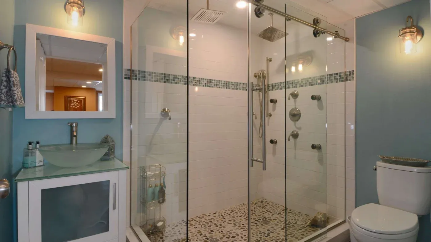 Modern bathroom featuring a glass-enclosed shower with pebble flooring and multiple showerheads, a vessel sink, and soft blue walls, creating a serene atmosphere.