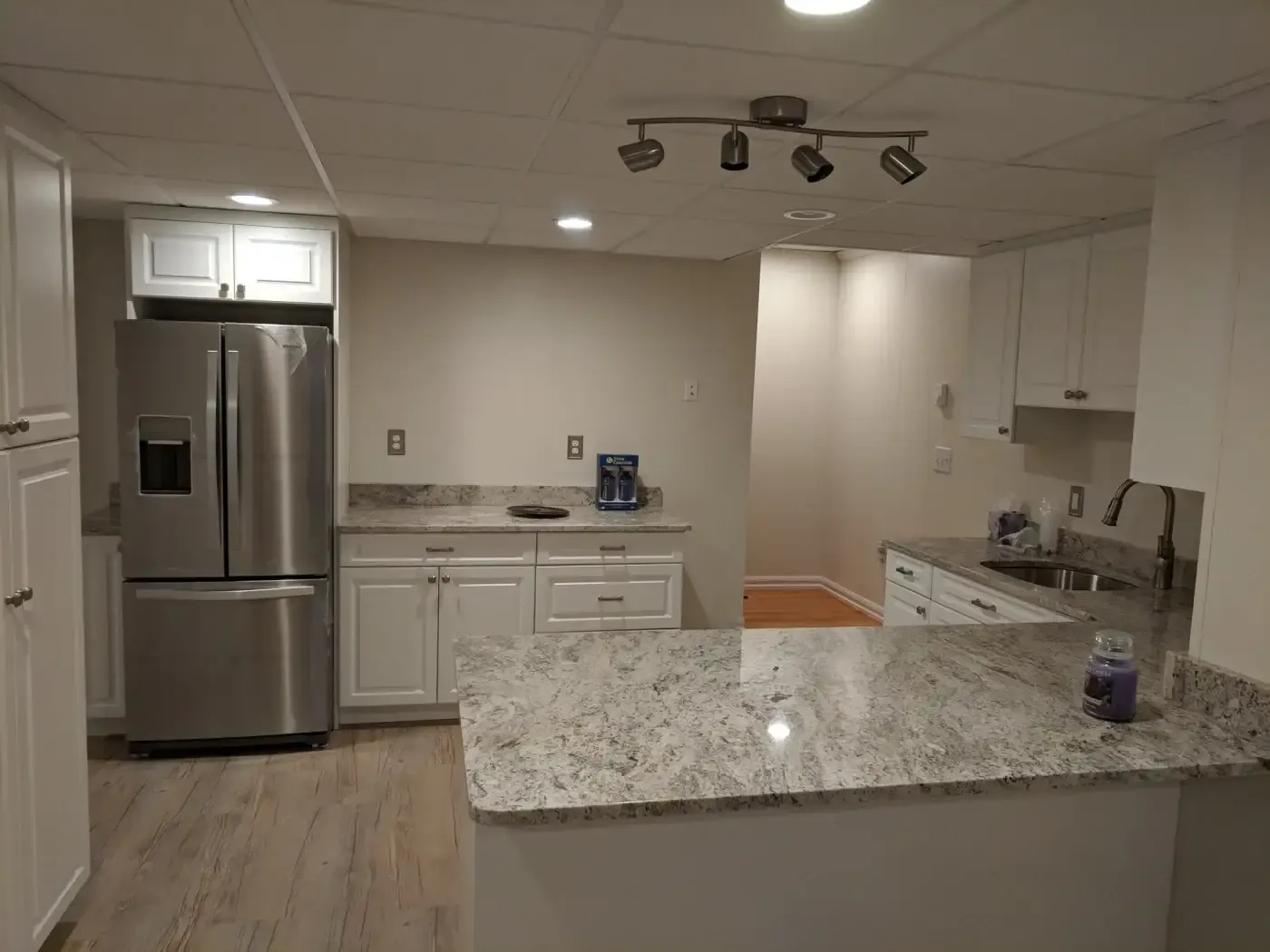 Modern kitchen with white cabinets, granite countertops, and stainless steel fridge. Recessed and track lighting create a cozy, welcoming atmosphere.