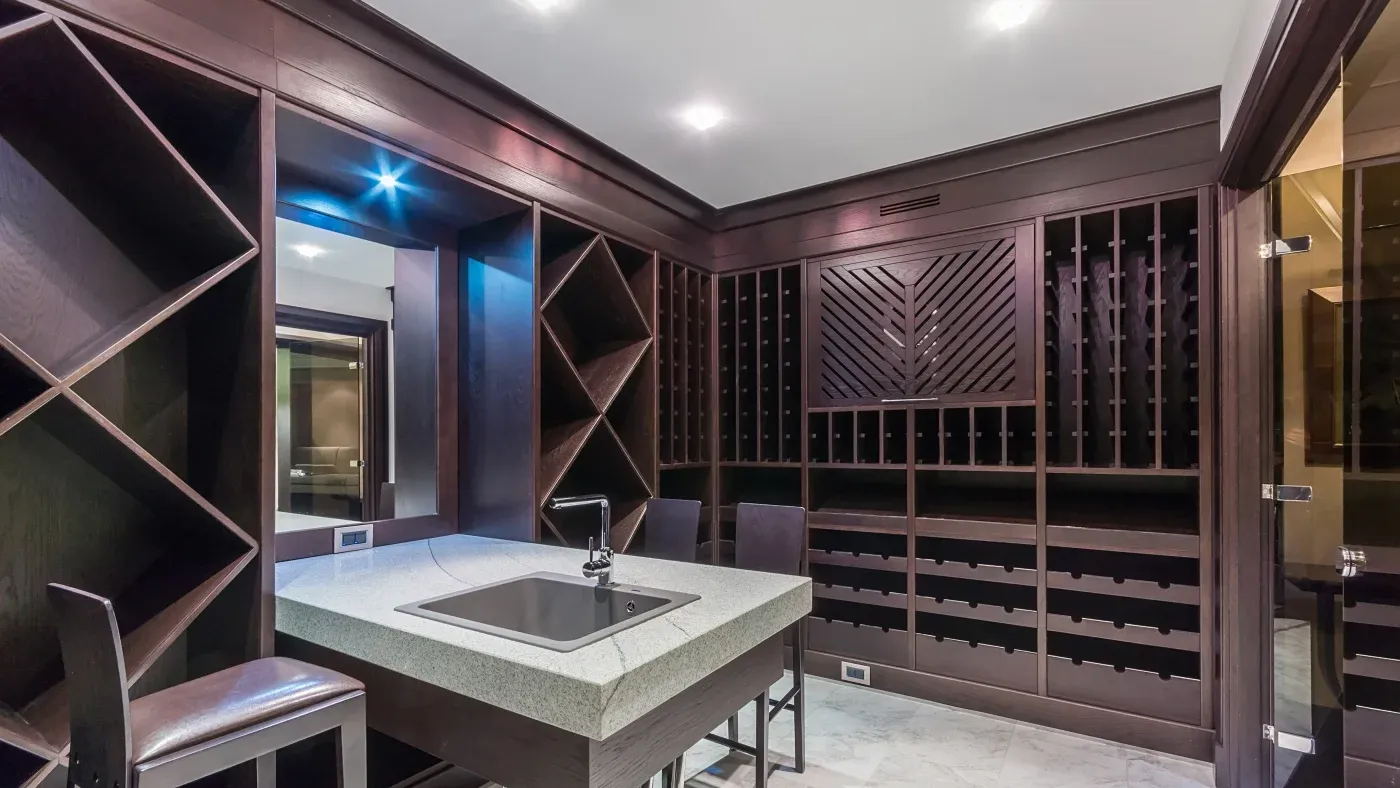 Luxurious wine cellar with dark wooden racks on the walls, a marble countertop island with a sink, and plush high chairs, conveying a sophisticated ambiance.
