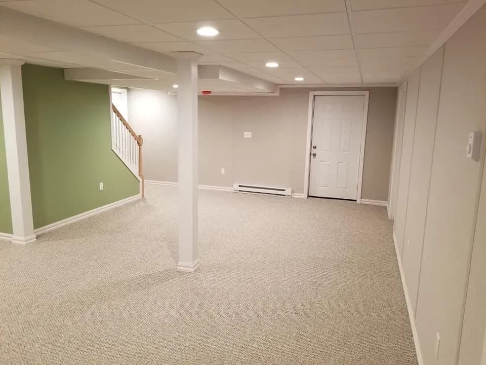 Spacious basement with beige carpet, light gray walls, and a green accent wall. Recessed lighting and a white door create a clean, inviting space.