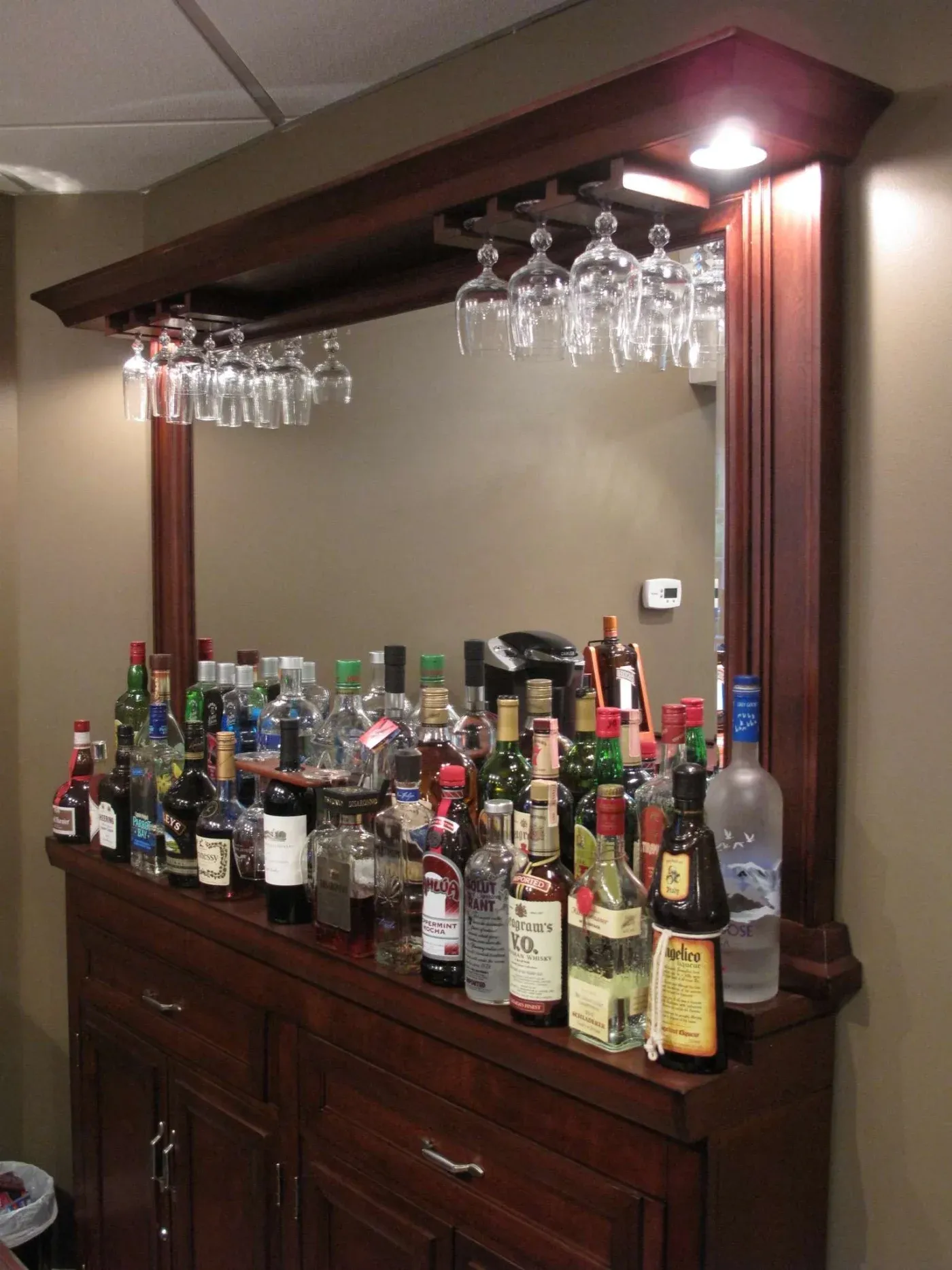 A home bar with a wooden cabinet loaded with assorted liquor bottles and mixers. Wine glasses hang upside-down above, reflecting a cozy ambiance.