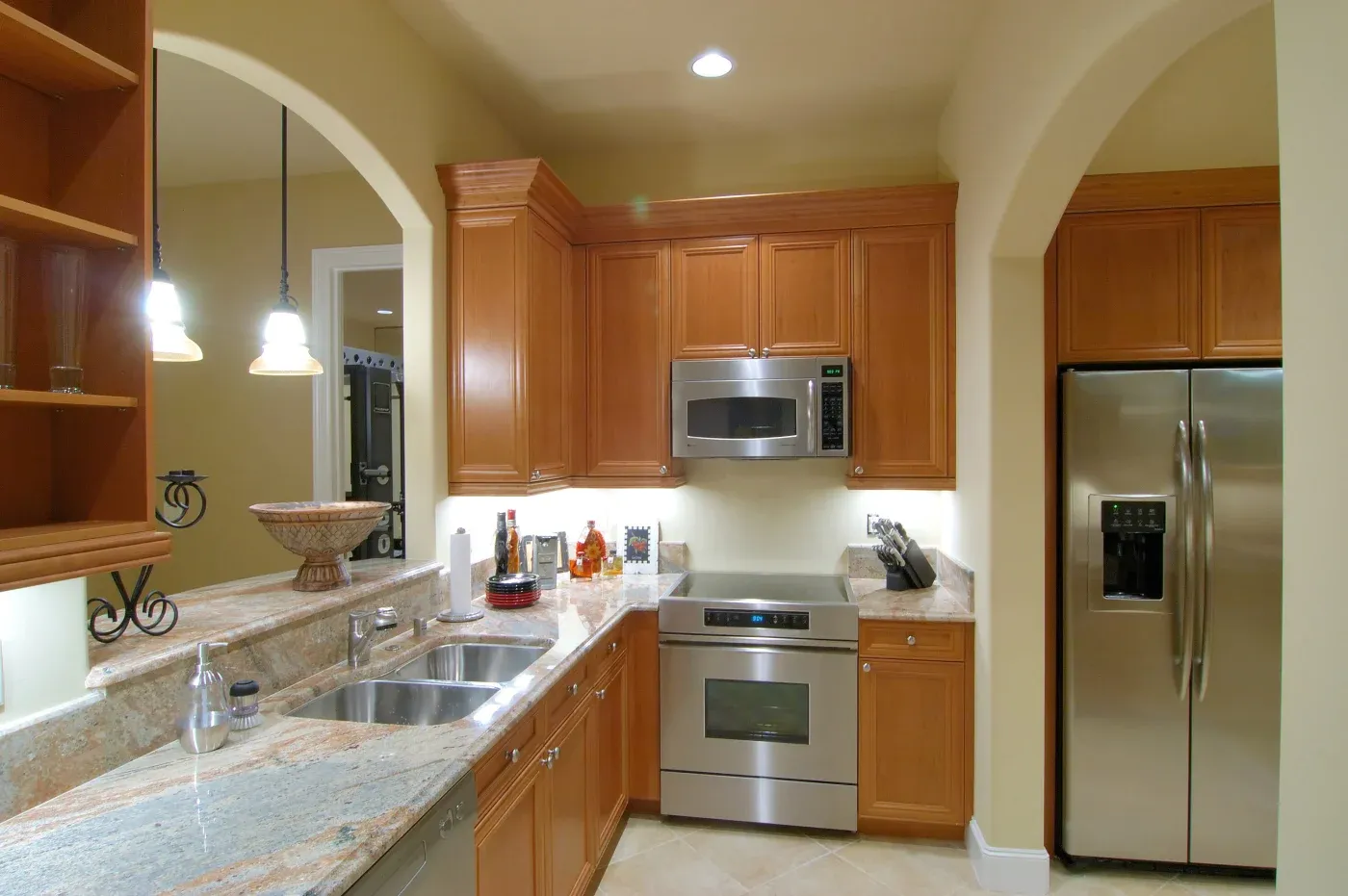 Warm kitchen with wood cabinets, stainless steel appliances, and granite countertops. Arched doorways and pendant lights enhance a cozy ambiance.