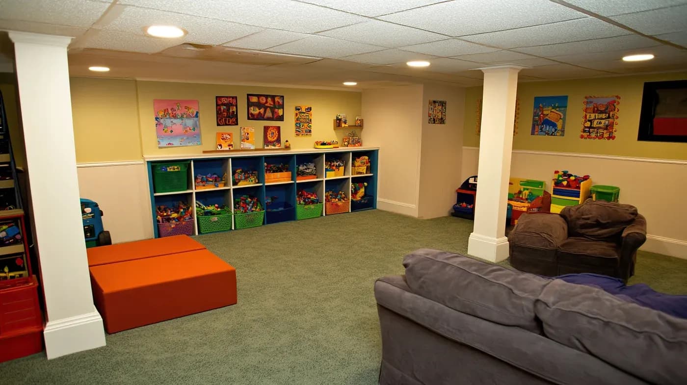 A brightly lit playroom with colorful wall posters, shelves filled with toys, and a cozy sofa. The room conveys an inviting and cheerful atmosphere.