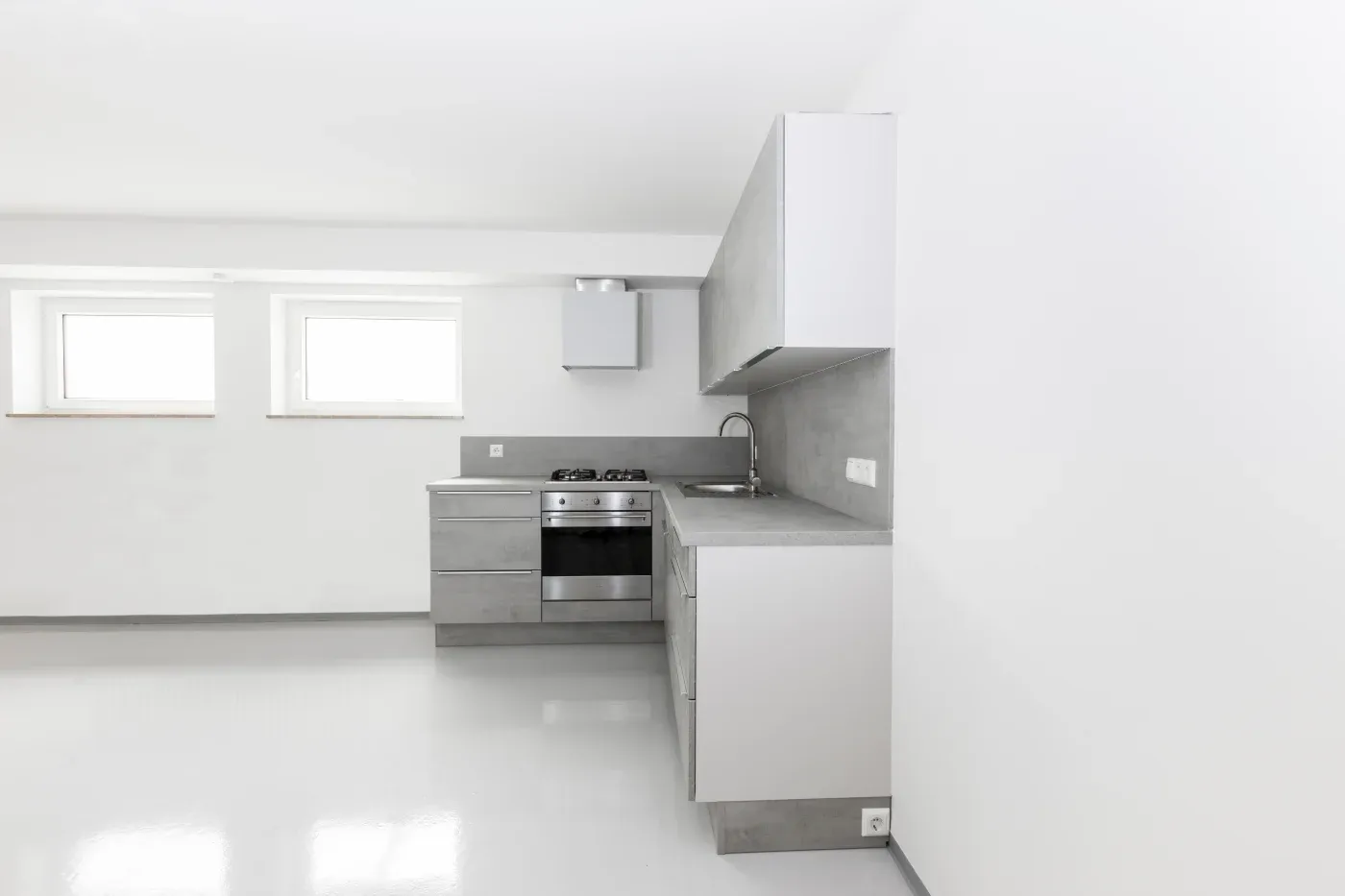 Minimalist kitchen with sleek gray cabinets, a stainless steel stove, and a sink. White walls and two small windows add brightness.