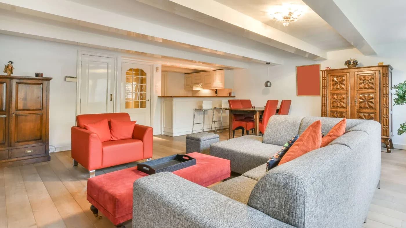 Spacious modern living room with gray sectional sofa, red armchairs, and matching ottomans. Neutral decor with wood accents and warm lighting.