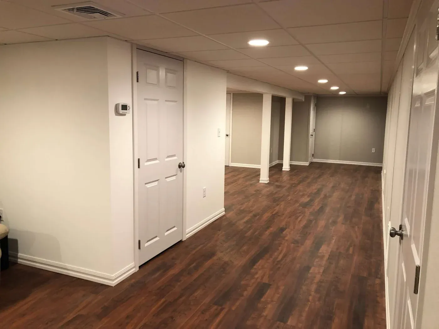 A spacious, empty basement with wooden flooring and white walls. Multiple recessed lights illuminate the area, creating a clean and new ambiance.
