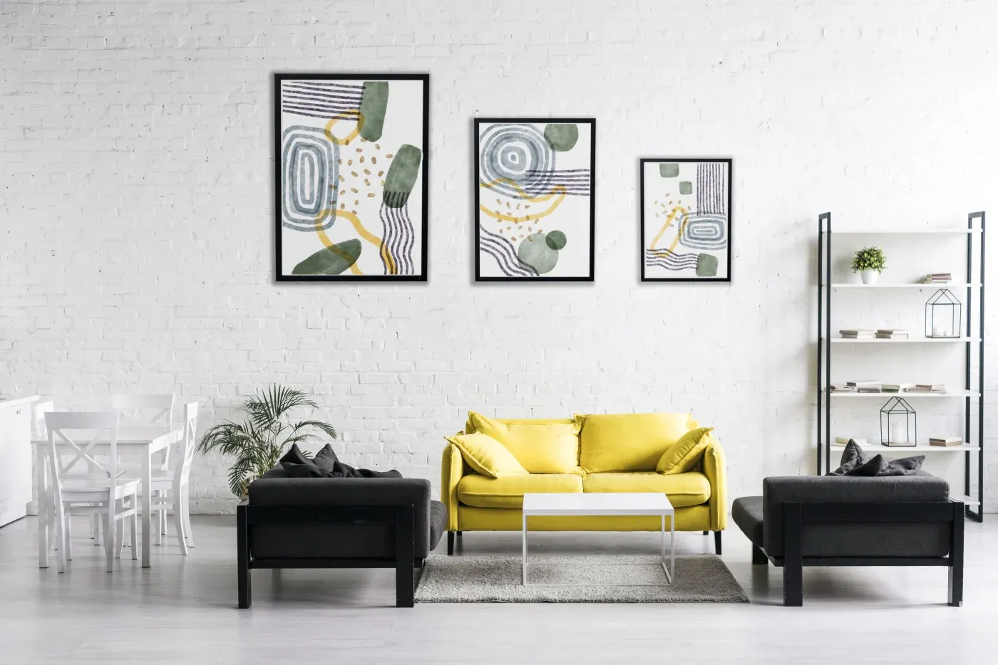 Modern living room with a yellow sofa, two black armchairs, and a white coffee table on a light gray rug. Three abstract art pieces on a white brick wall.