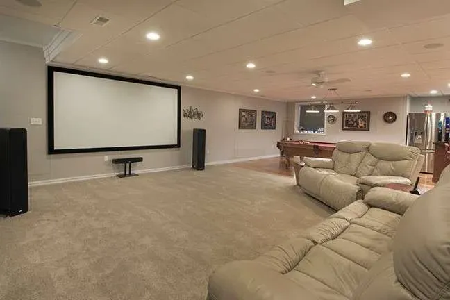 A spacious home theater with a large screen, leather recliners, surround sound speakers, and a pool table in the back, creating a cozy entertainment vibe.