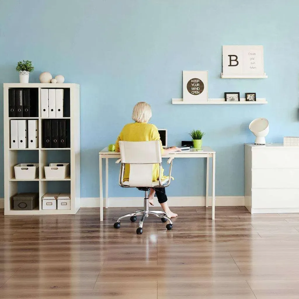 A person sits at a modern desk in a minimalist home office. Shelves and decor adorn light blue walls. The room exudes calm and organization.