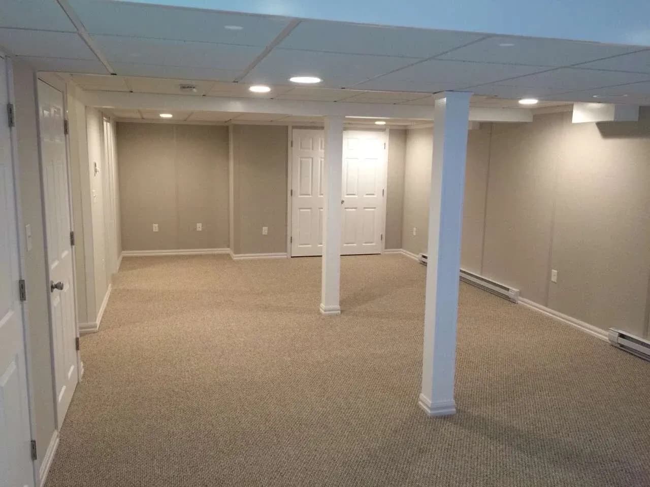 Finished basement with carpeted flooring, white support columns, recessed lighting, multiple doorways, and electrical outlets on beige walls