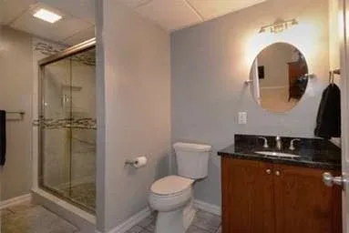 Modern bathroom with a glass-enclosed shower, white toilet, and dark wood vanity with a black countertop. Soft lighting creates a clean, cozy ambiance.