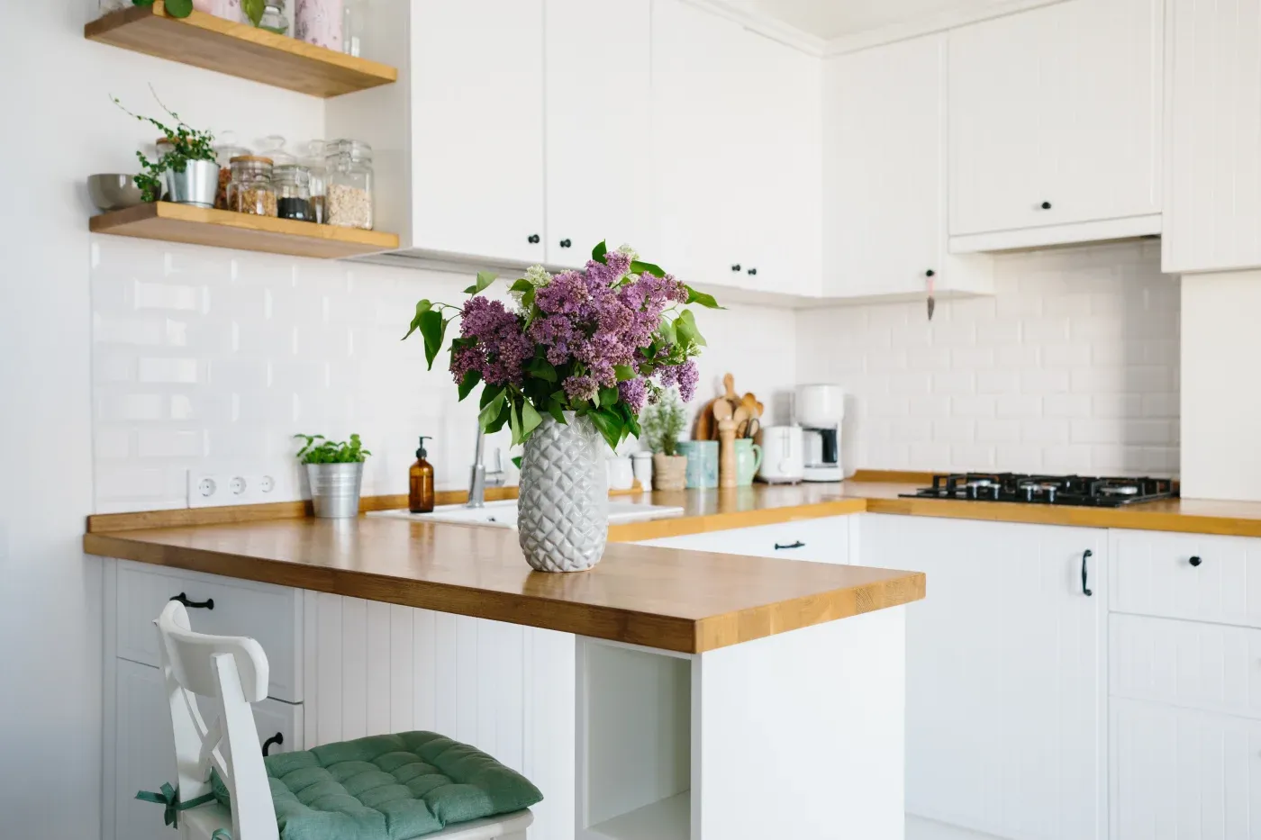 Bright kitchen with white cabinets and wood countertops. A vase with purple flowers on a central island adds a fresh, inviting touch.