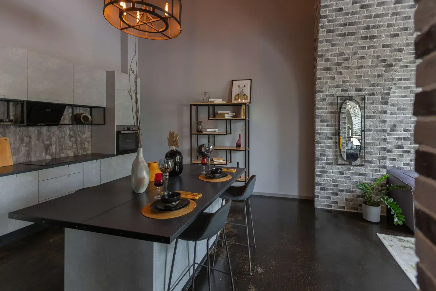 Modern kitchen with industrial decor, featuring a black dining table set with dark dishes, brick accent wall, open shelving, and pendant lighting. Cozy and minimalist.