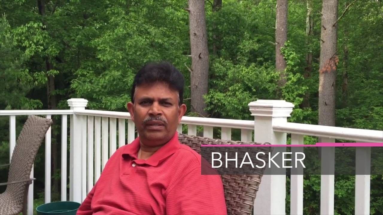 A man in a red shirt sits on a deck chair with a serene forest background. White railing surrounds the deck, creating a calm, outdoor setting.