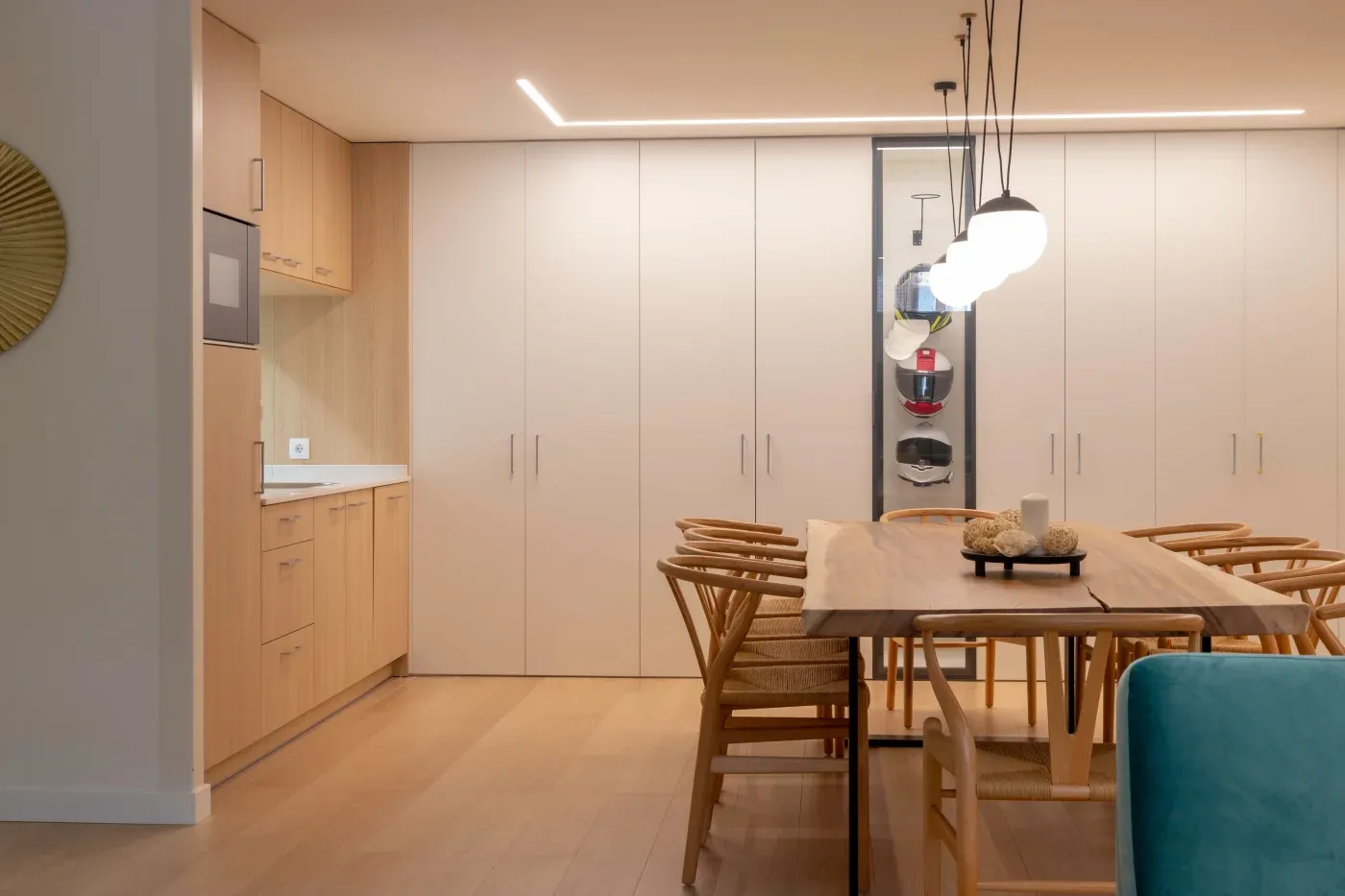 Modern dining area with a wooden table, wicker chairs, and pendant lights. Minimalist kitchen in light wood tones. Calm and inviting ambiance.
