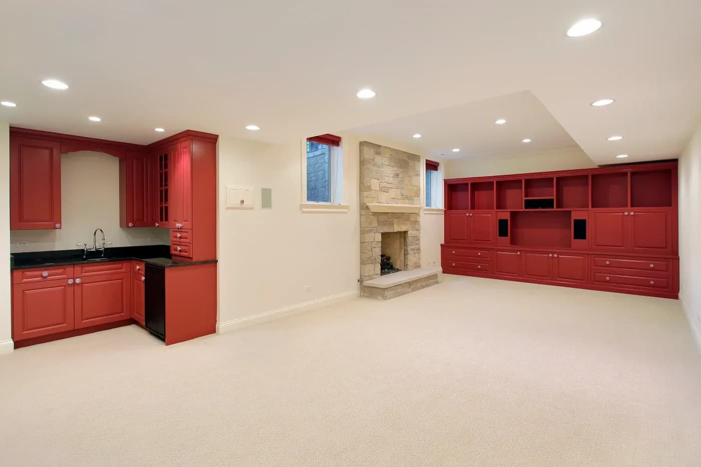 Spacious basement with cream carpet, beige stone fireplace, red built-in cabinets and wet bar, exuding a warm, inviting ambiance.