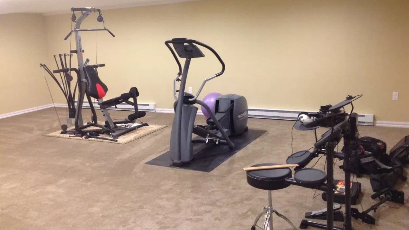 Home gym and music room featuring exercise equipment and a drum set on beige carpet. Neutral walls create a calm, multi-purpose space.