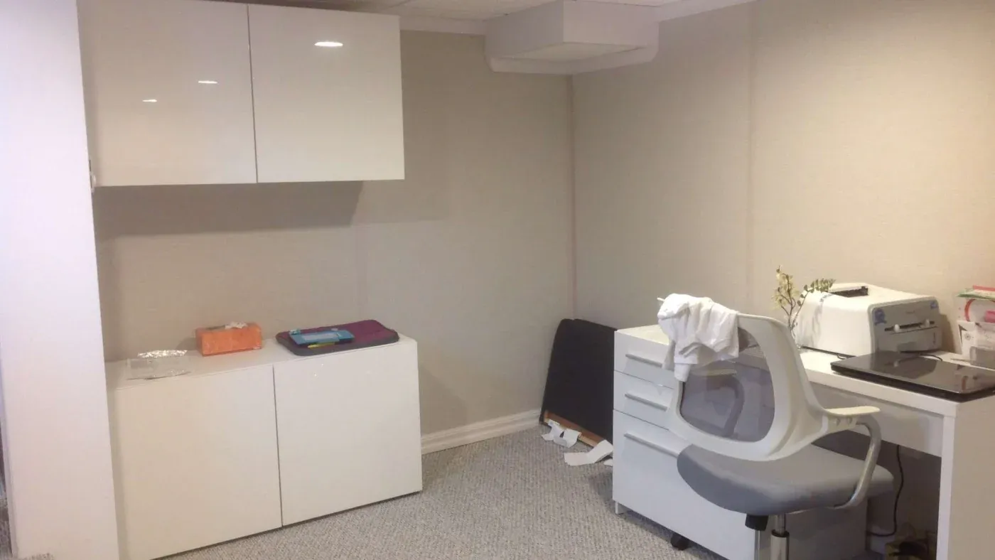 A tidy, minimalist office with white cabinets, a gray chair, and a printer on a desk. Soft lighting and neutral walls create a calm, organized atmosphere.