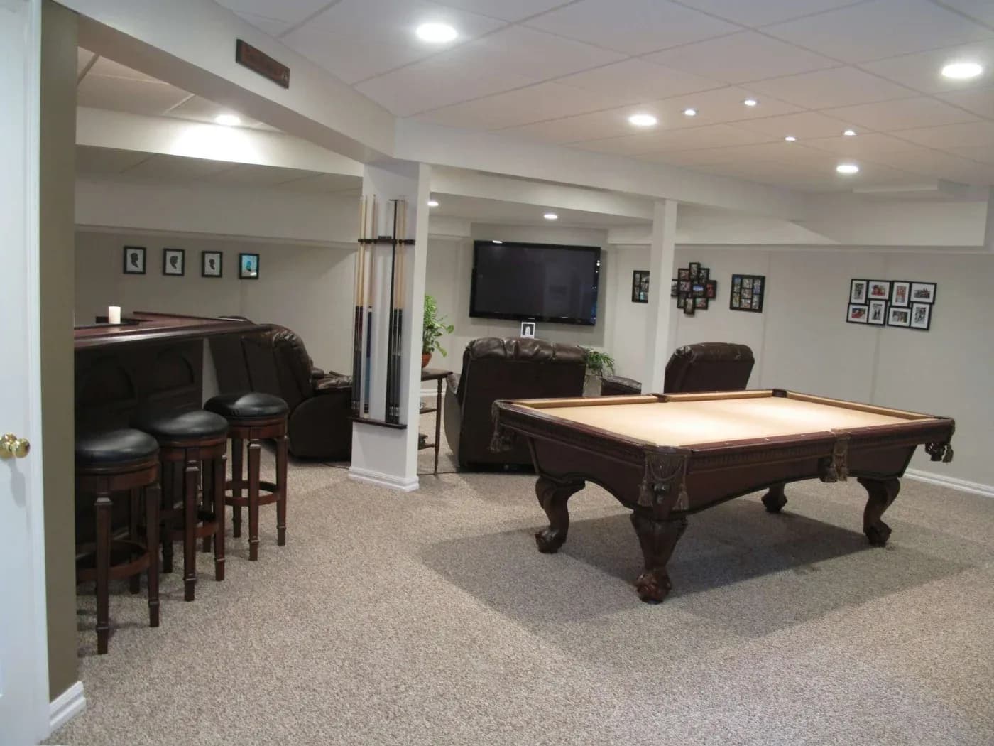 Spacious basement rec room with a pool table, bar stools, leather seating, and framed photos on the walls. The ambiance is cozy and inviting.