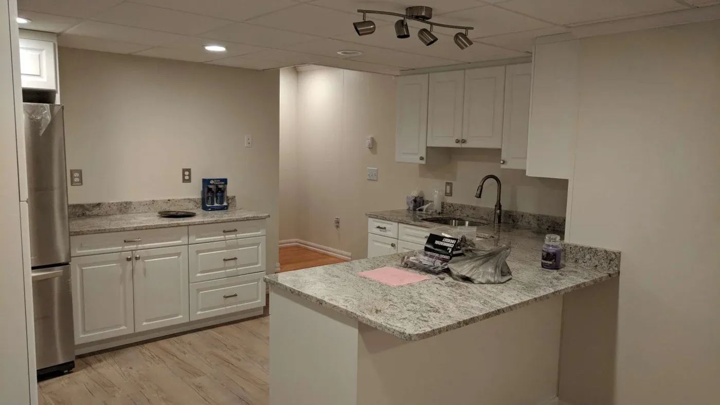 A modern kitchen features white cabinets, granite countertops, and stainless steel appliances. The space is well-lit with track lighting, creating a clean and inviting atmosphere.