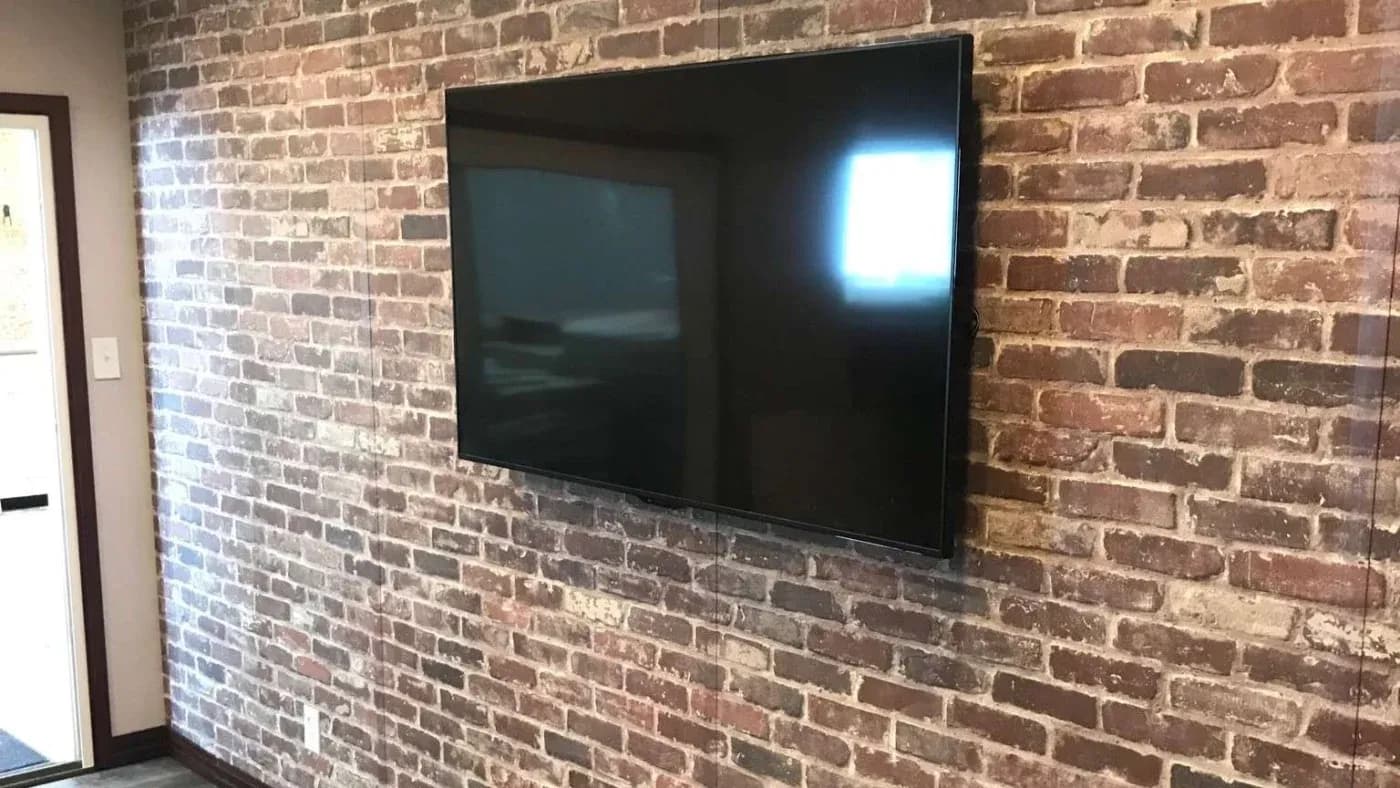 A sleek, modern flat-screen TV is mounted on a rustic, exposed brick wall. The room has a cozy, industrial feel with soft natural light.