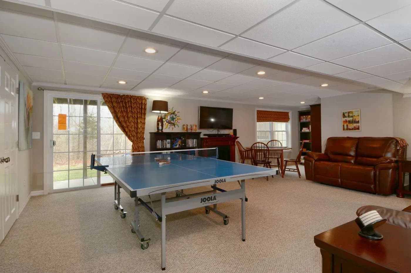 Spacious basement with a ping pong table, leather couch, TV, and dining table. Sliding glass doors lead outside, creating a cozy recreation area.