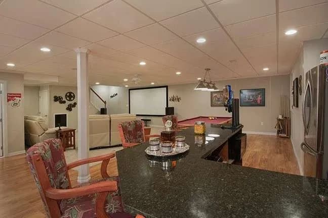 Spacious entertainment room with a bar, bar stools, pool table, and theater seating. Modern decor, warm lighting, and a cozy, inviting atmosphere.