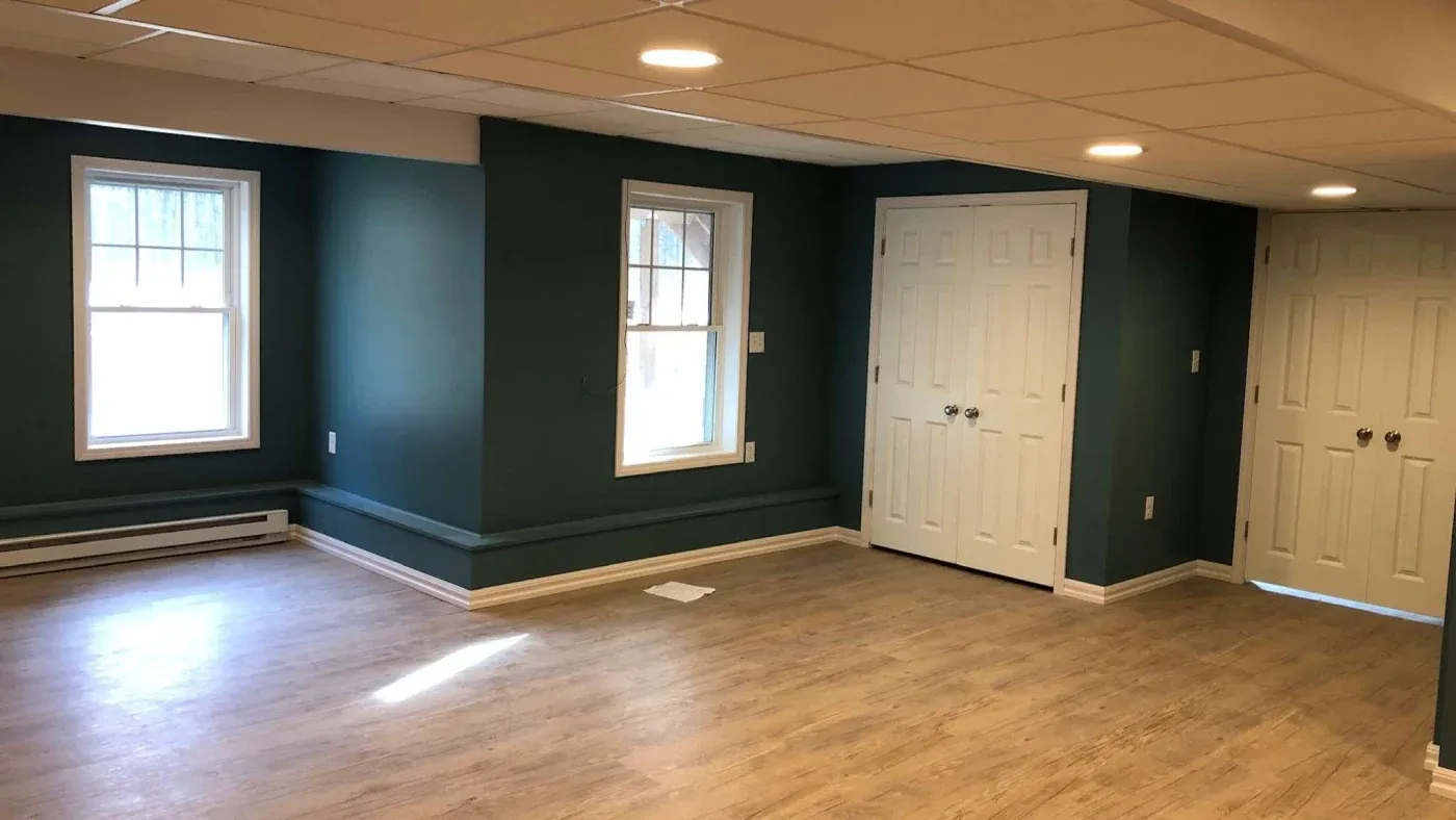 Spacious basement with teal walls, light wood flooring, and recessed lighting. Two windows on the left, white double closets on the right. Bright, clean ambiance.