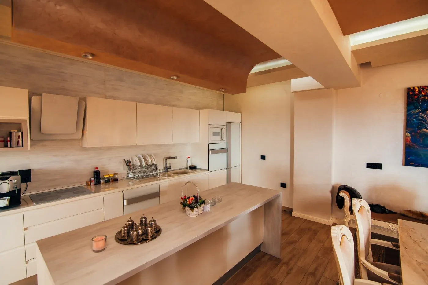 Modern kitchen with brown and white tones, featuring sleek cabinets, an island with trays and a candle, and a warm, inviting atmosphere.