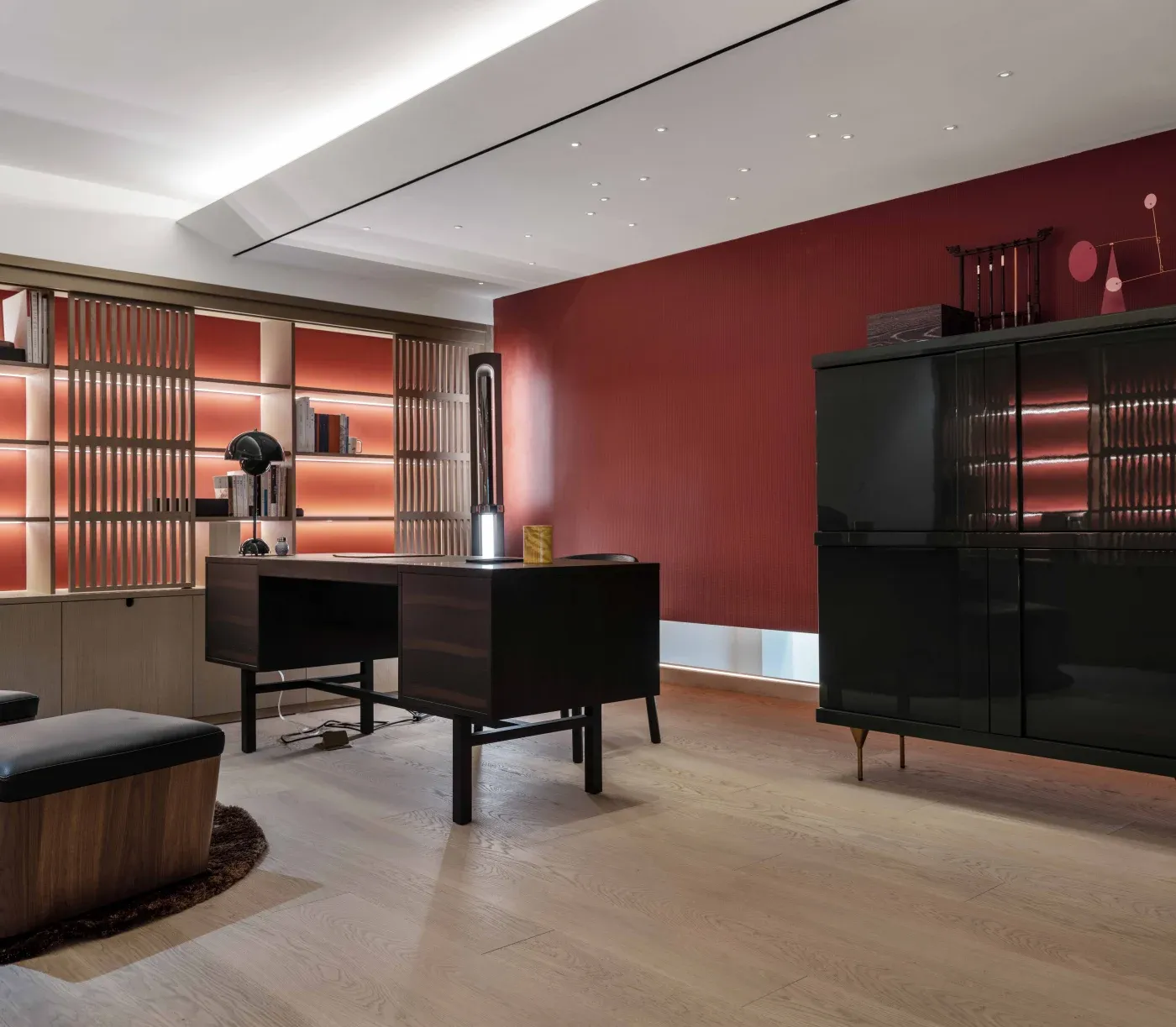 Modern office space with a dark wood desk, sleek black cabinets, and warm ambient lighting. Red accent wall and wooden flooring create a cozy atmosphere.