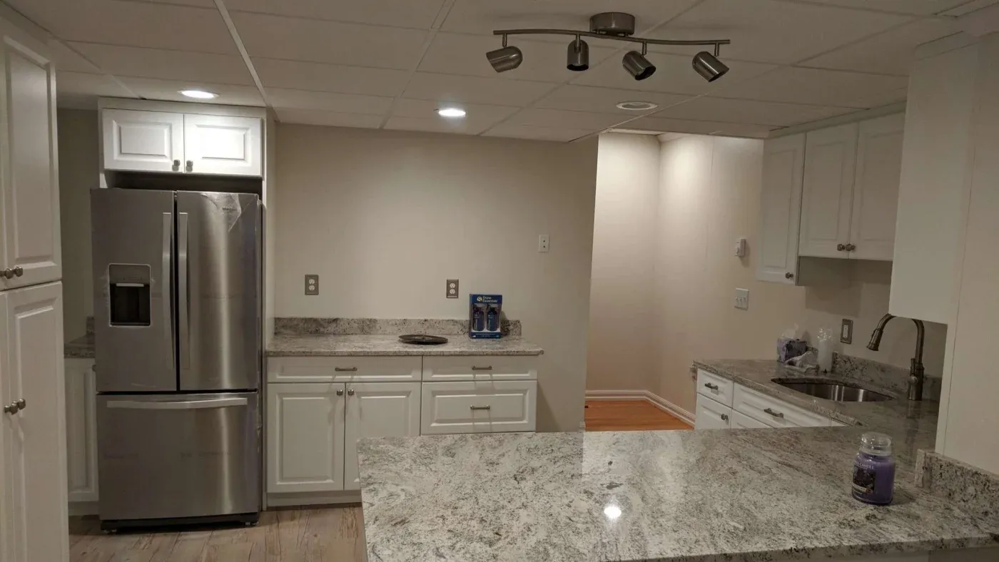 Modern kitchen with stainless steel fridge, granite countertops, and white cabinetry. Soft lighting creates a clean and inviting atmosphere.