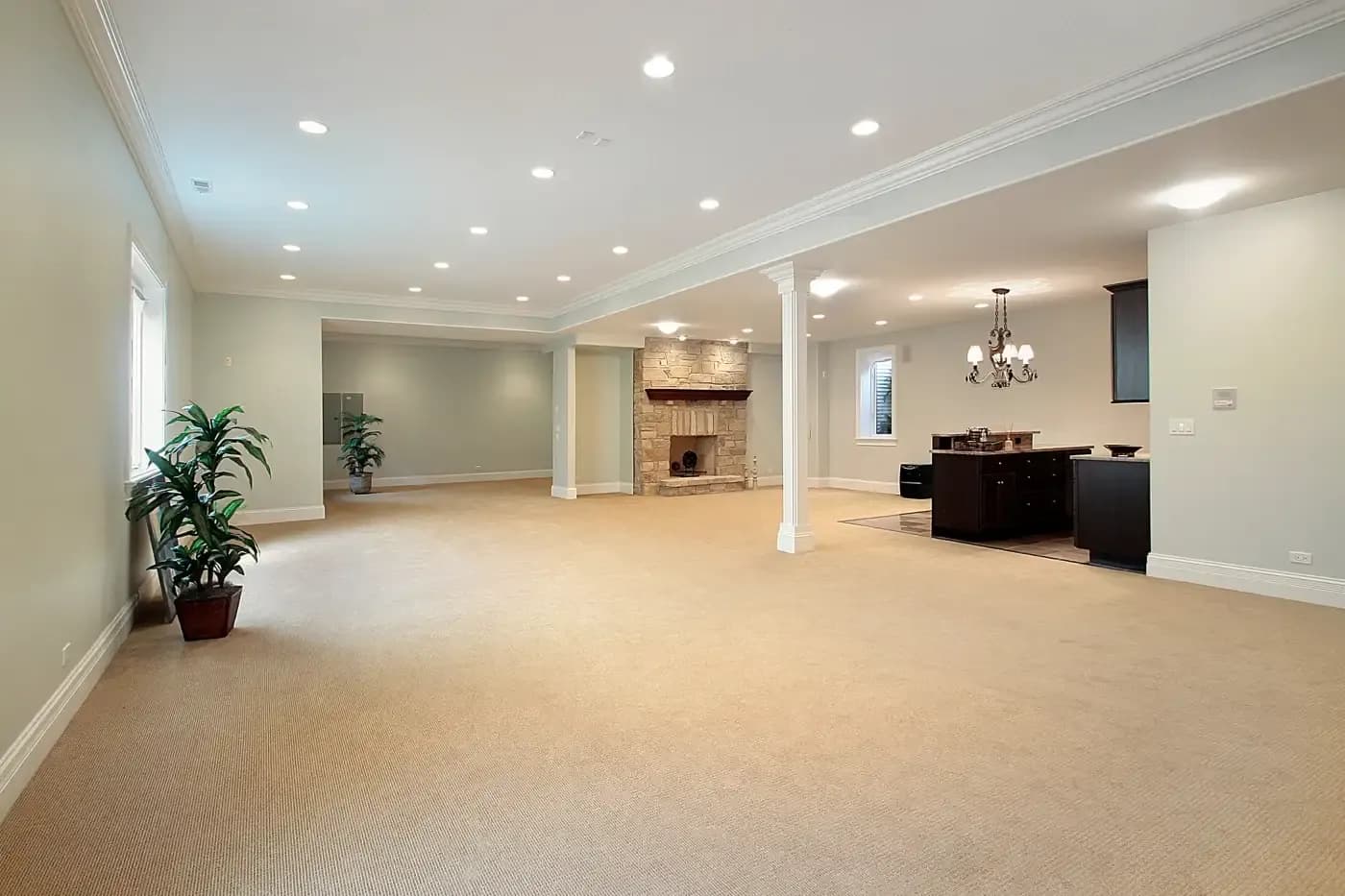 Spacious basement with beige carpet, light green walls, and a stone fireplace. Recessed lighting and a chandelier illuminate the open, inviting space.