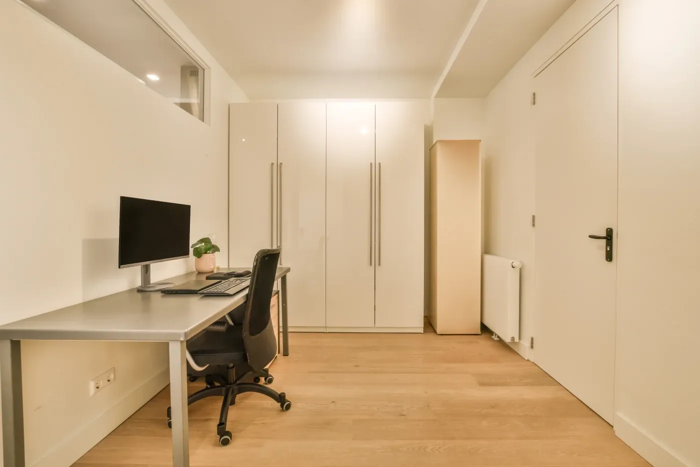 Minimalist office with a sleek desk, computer, and chair. Neutral tones and smooth floors create a calm, organized workspace setting.