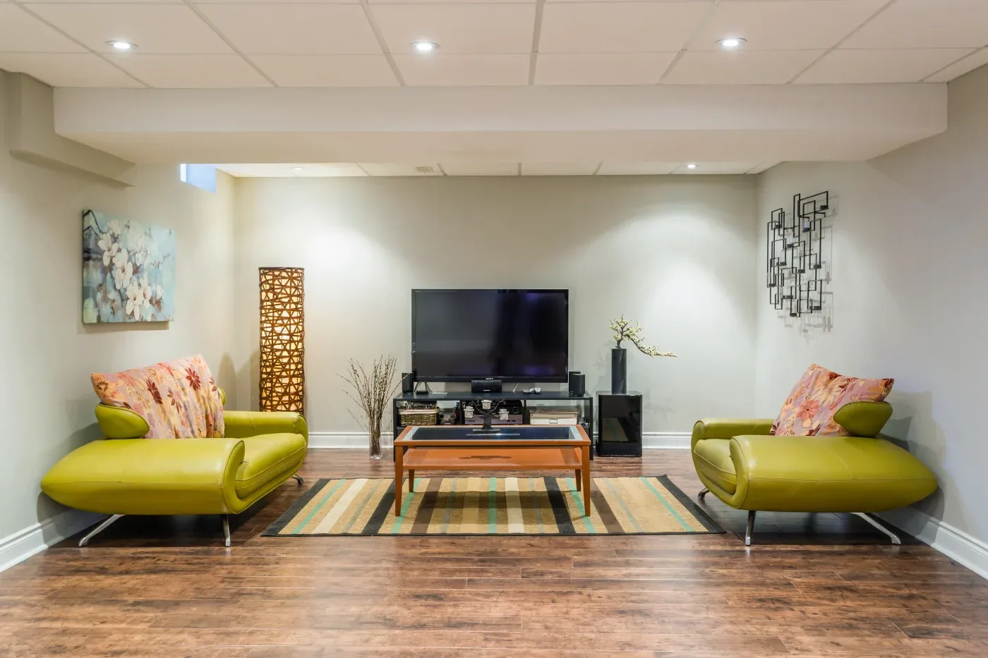 Modern living room with lime green sofas, a flat-screen TV on a stand, and a wooden coffee table. Decor includes abstract wall art and patterned cushions.