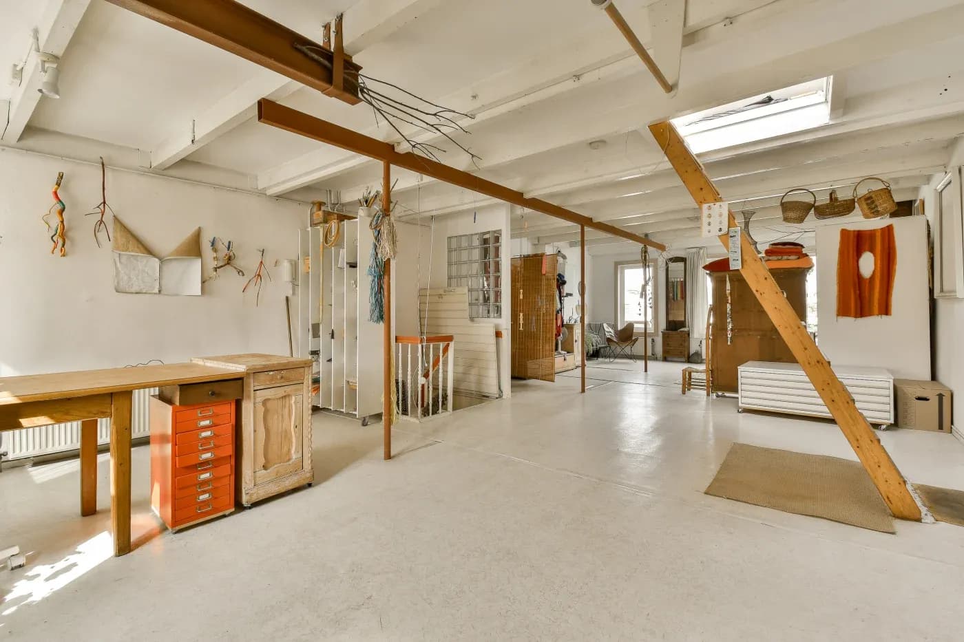Open, airy studio with white walls and beams, wooden furniture, colorful textiles, and woven baskets. The space feels creative and inviting.