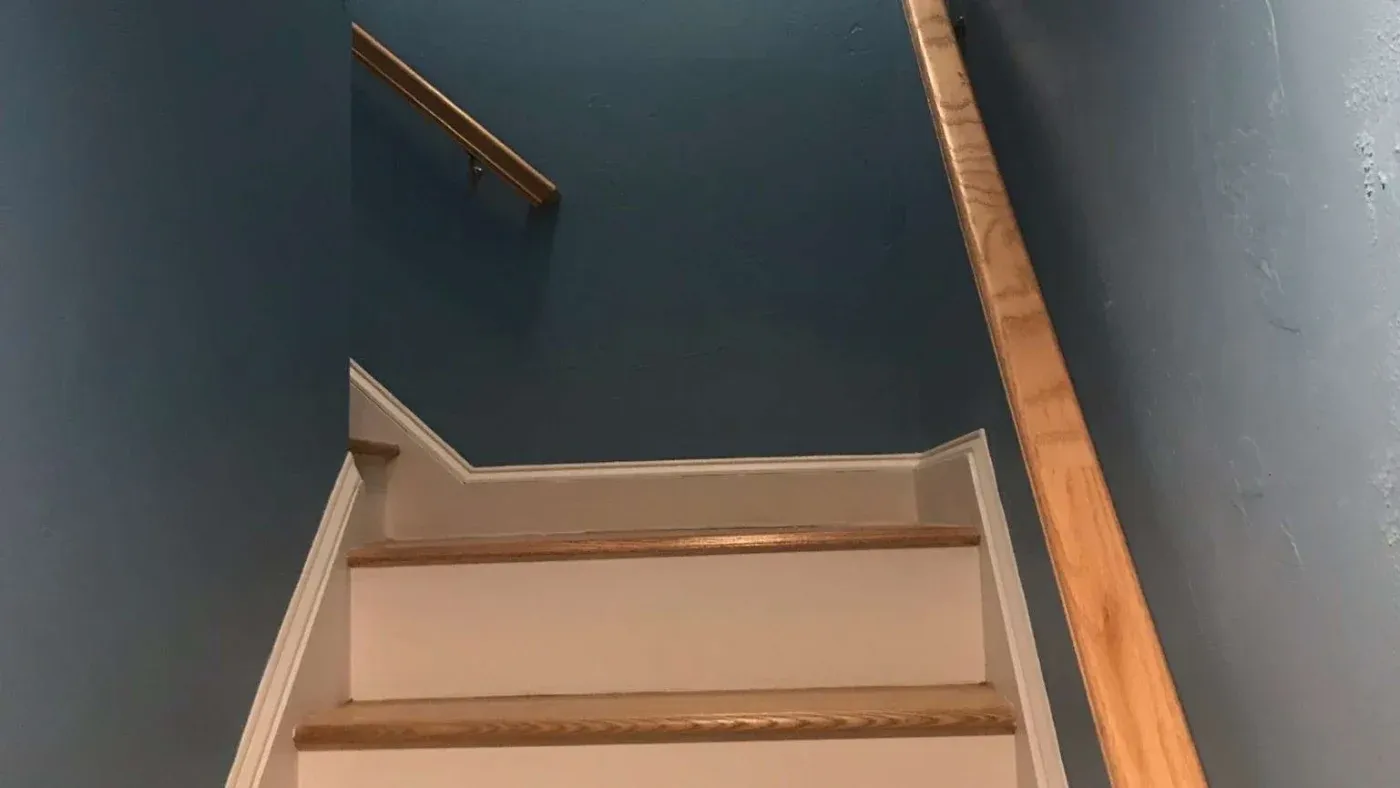 A staircase with light wood steps and railings ascends between blue walls. The scene appears calm and orderly, suggesting a quiet indoor setting.
