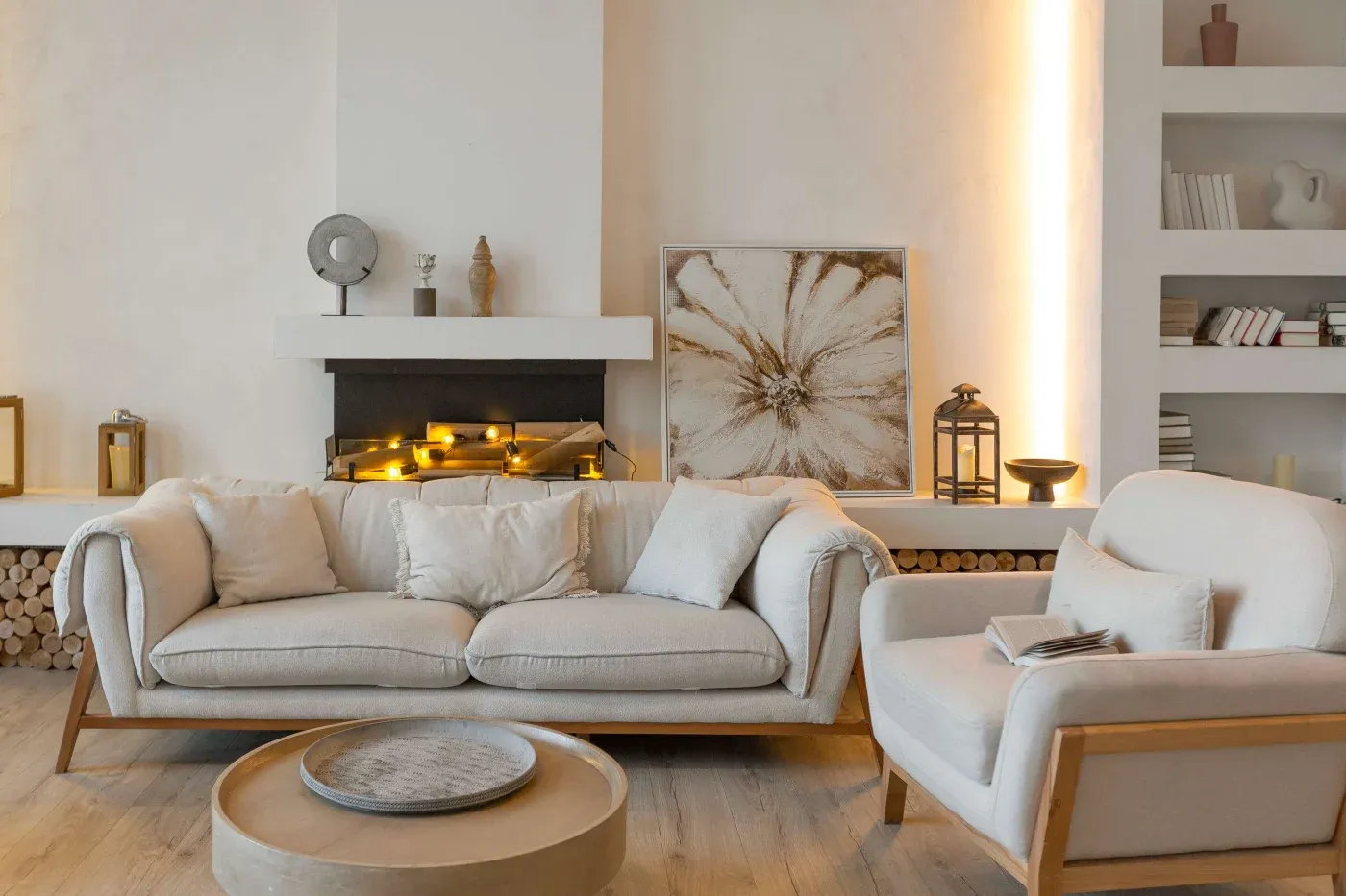 Cozy living room with neutral tones featuring a beige sofa and armchair, elegant wall art, a modern fireplace with soft lighting, and decorative shelves.