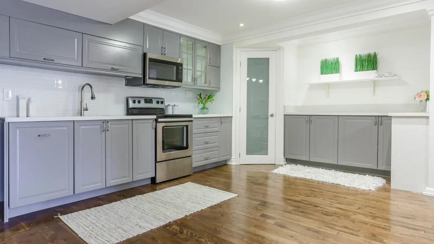 Bright, modern gray kitchen with stainless-steel appliances, white tile backsplash, wood floors, and a clean, inviting open layout.