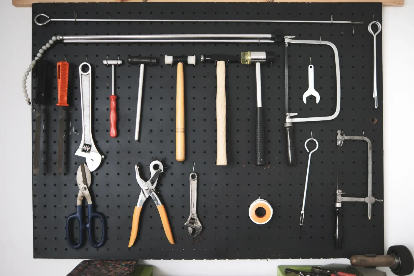 A black pegboard displays various tools, including pliers, wrenches, hammers, and saws, organized neatly. The setup conveys readiness and efficiency.
