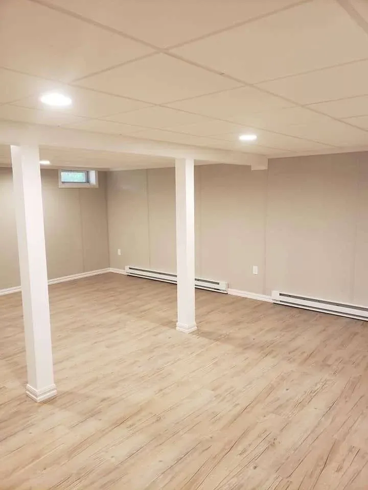 Bare, renovated basement with light wood flooring, beige walls, recessed lighting, and heating on baseboards. The space conveys a clean, minimalist feel.