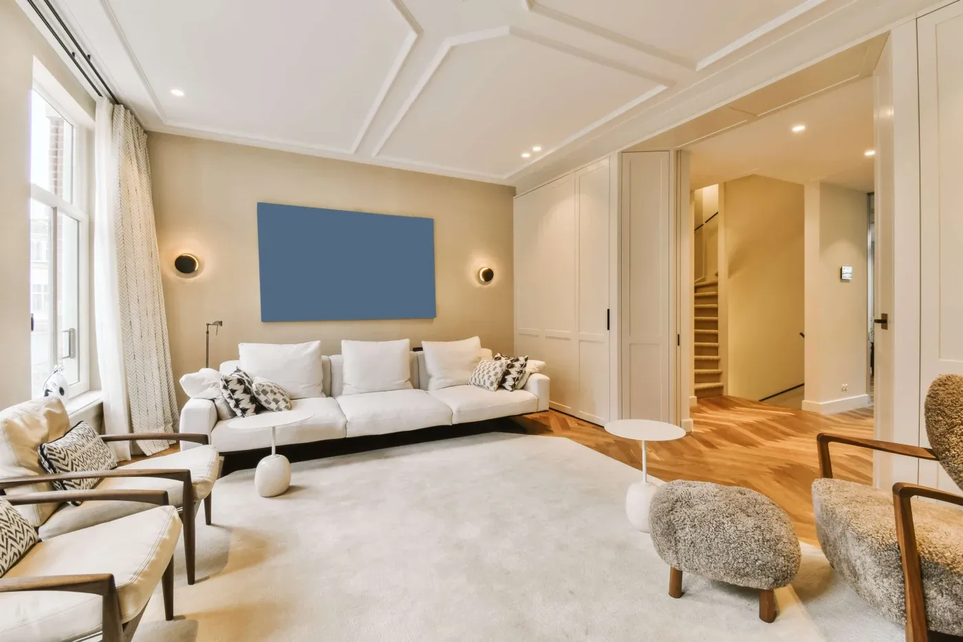 Cozy living room with neutral tones featuring a beige sofa and armchair, elegant wall art, a modern fireplace with soft lighting, and decorative shelves.